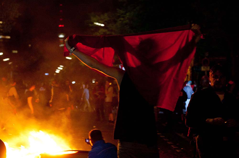 Guy with red flag standing near a burning trash bin in Berlin on May 1st 2012