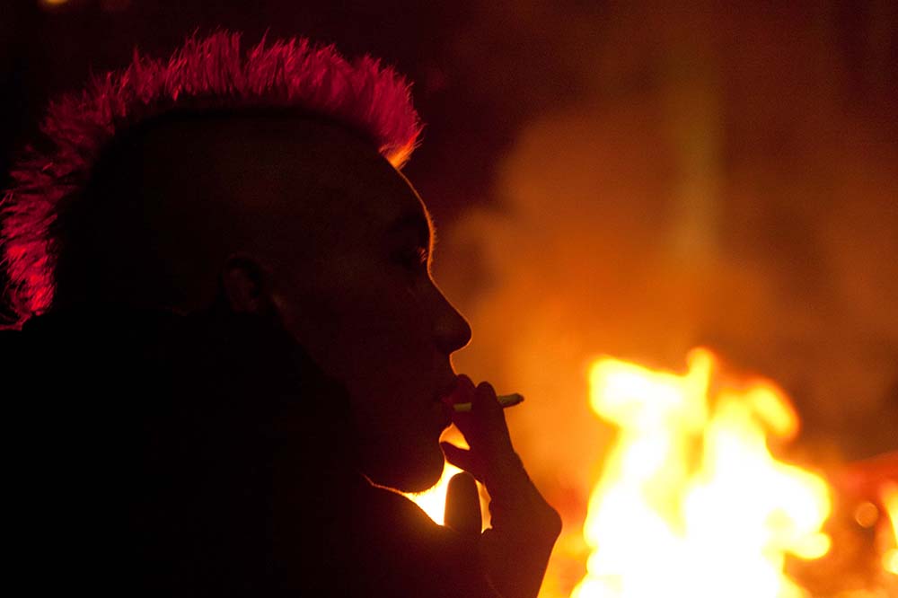 Punk with mohican smoking while sitting close to a burning trash bin in Berlin on May 1st 2012